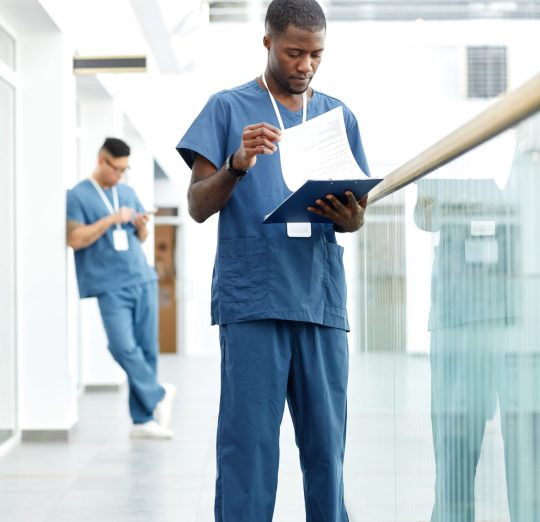 Vertical full length portrait of young African American doctor holding clipboard while standing in hall of modern clinic
